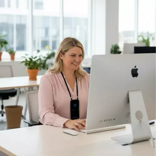 Девушка работает за компьютером в офисе, на груди висит прибор БРТ WebWellness LifeBalance